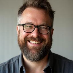 Portrett av Erik Hansen, en blid mann med skjegg og briller